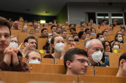 Several people are sitting in a lecture hall. Some people are wearing masks.