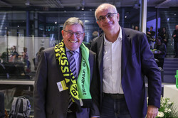 Photo: Two people stand side by side, one wearing a black-yellow-green scarf with the inscription “Borussia Dortmund” and “Technische Universität Dortmund.”