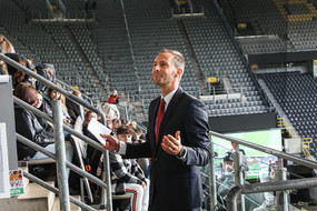 A man in a suit gives a speech to freshman students in a soccer stadium.