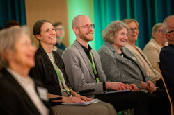 Christin Olschewsky und Andreas Bierwald vom Team Deutschlandstipendium sitzen im Publikum und verfolgen das Programm der Feier im Bühnenbereich