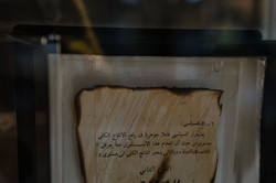 Ein angebranntes Schriftstück aus der Universitätsbibliothek Mossul hinter einer Glasscheibe