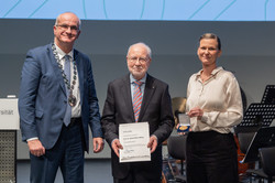 Das Bild zeigt Bayer, Müller-Böling, Flatten, welche nebeneinanderstehend in die Kamera lächeln. Müller-Böling hält eine Urkunde für eine weitere Universitätsmedaille in seinen Händen.