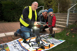In the foreground of the image, a drone can be seen on a poster-like background. Behind it are two adults and a child.