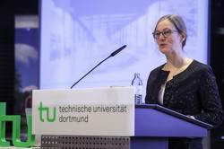 Foto: Eine Person spricht am Rednerpult der Technischen Universität Dortmund vor einer Leinwand mit einer Präsentation.