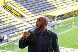 A man holding a microphone sings in front of a stand in a soccer stadium.