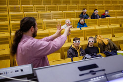 People wearing protective goggles in a lecture hall. In the foreground a man explaining something.