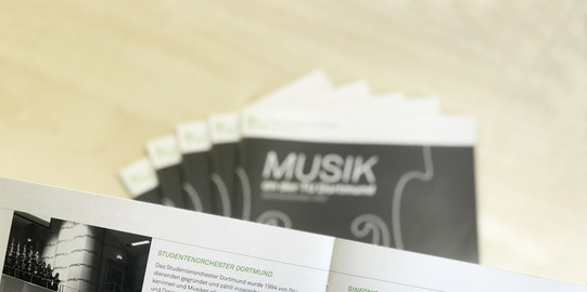 Musikbroschüre aufgeklappt, im Hintergrund weitere Broschüren