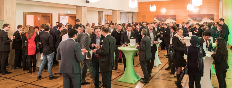 Teilnehmerinnen und Teilnehmer der Stipendienfeier stehen an Stehtischen in großem Veranstaltungsraum