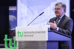 Photo: A person speaks at the podium of TU Dortmund University in front of a screen displaying a presentation.