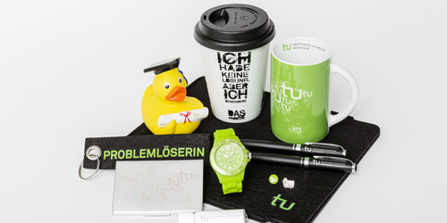 Verschiedene Merchandise-Artikel der TU Dortmund, unter anderem eine Tasse, eine Uhr und ein Schlüsselanhänger, liegen auf einem Tisch