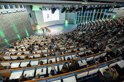 Foto: Blick von oben in einen großen, gefüllten Hörsaal der Technischen Universität Dortmund, in dem zwei Personen eine Präsentation vor Publikum halten.