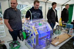 Four people stand behind a 3D printer.