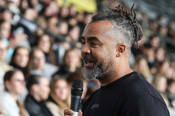Patrick Owomoyela speaking into a microphone. In the background you can see the stands filled with first-year students.