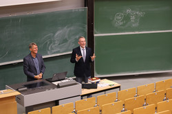 Zwei Männer stehen vor der Tafel in einem Hörsaal
