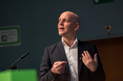 A man is giving a speech, a microphone can be seen in front of him.