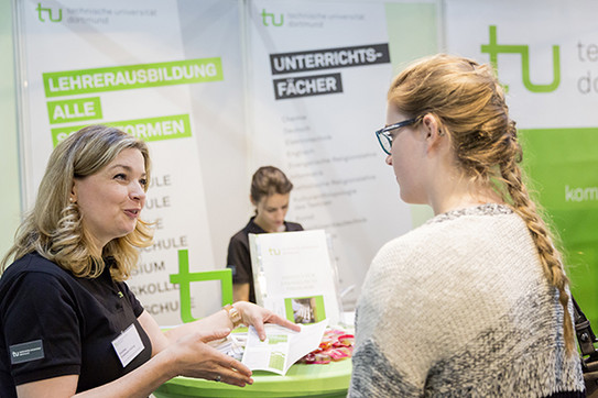 Three women at the exhibition booth of TU Dortmund University
