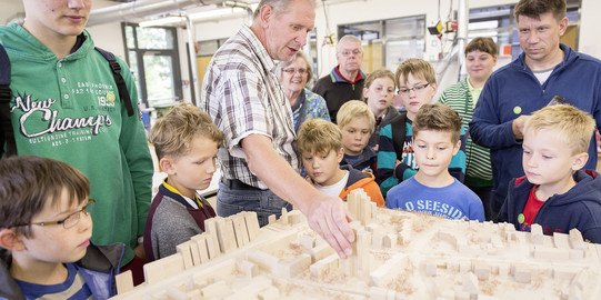 Kinder und Erwachsene stehen rund um ein Modell einer Stadt.