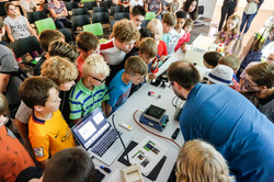 KinderUni-U Kinder stehen um einen Tisch herum, auf dem ein Experiment aufgebaut ist.