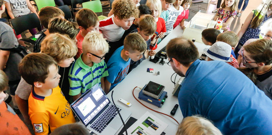 Kinder stehen um einen Tisch herum, auf dem ein Experiment aufgebaut ist.