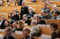 Several people are sitting in a lecture hall, one person is holding a microphone.