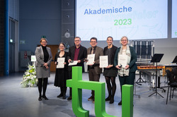 Lehrpreisträger*innen stehen mit ihren Medaillen und Urkunden auf der Bühne im Audimax zusammen mit Prorektorin Studium und Lehre Prof. Möhring