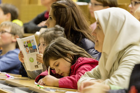 Kinder und Eltern internationaler Herkunft lauschen der Vorlesung im Hörsaal