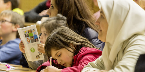 Kinder und Eltern internationaler Herkunft lauschen der Vorlesung im Hörsaal