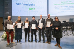 Das Bild zeigt ein Gruppenfoto der Gewinner*innen des Lehrpreis in der Kategorie mit über 60 Teilnehmenden. Die Gewinner*innen halten Urkunden in ihren Händen und lächeln in die Kamera. Im Hintergrund ist eine zweigliedrige Präsentation zu sehen.